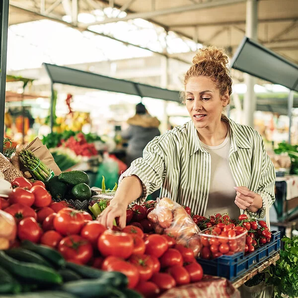 Eine Frau greift auf dem Markt nach frischen Tomaten.