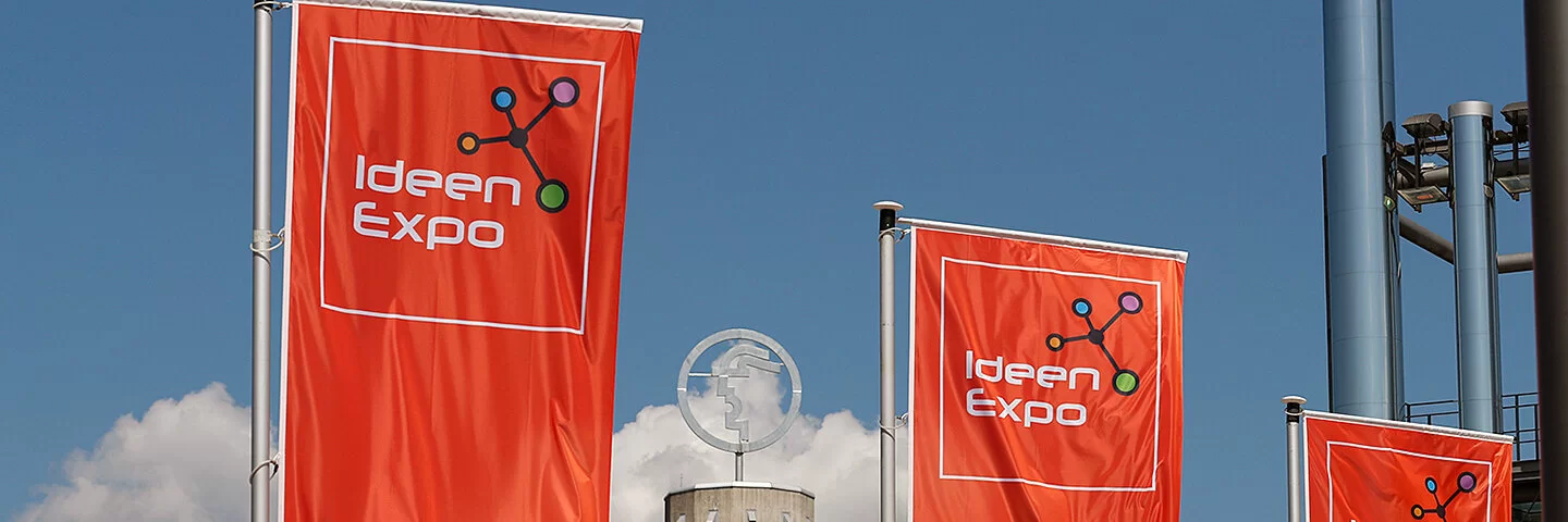 Drei rote Flaggen mit dem Logo der Ideenexpo wehen vor dem Eingang der Hannover Messe.