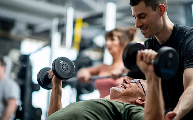 Ein Trainer zeigt einem Fitness-Anfänger Übungen mit Hanteln.