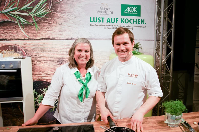 Die Moderatoren der AOK-Kochshow in Balingen stehen in der Küche und schauen in die Kamera.