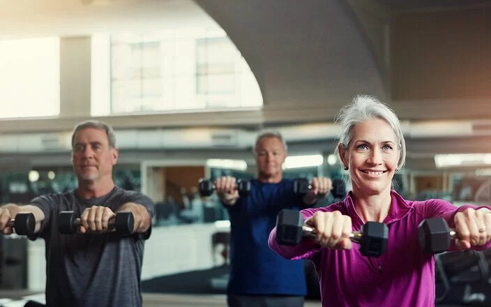Ältere Menschen trainieren mit Kurzhanteln in einem Fitnessstudio.