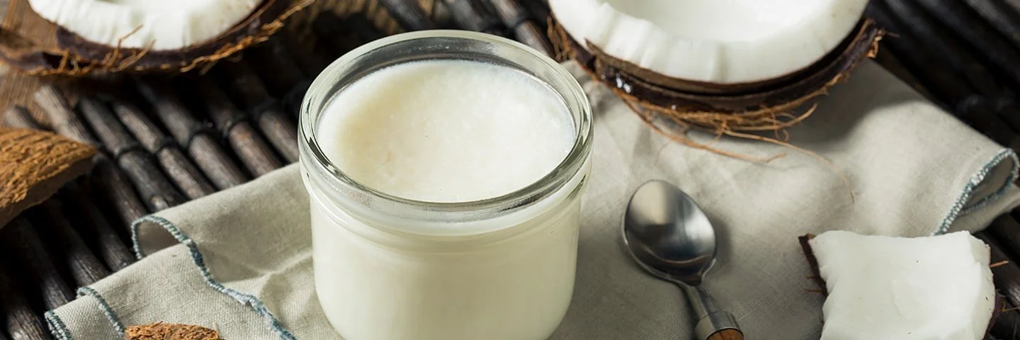 Ein Glas mit festem Kokosöl und eine aufgebrochene Kokosnuss liegen auf einem Tisch.