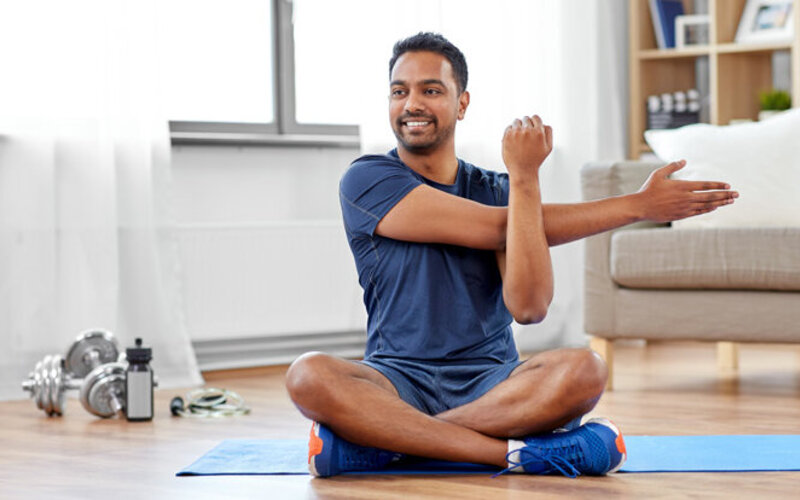 Ein junger Mann macht in seinem Wohnzimmer Gymnastikübungen und lacht.