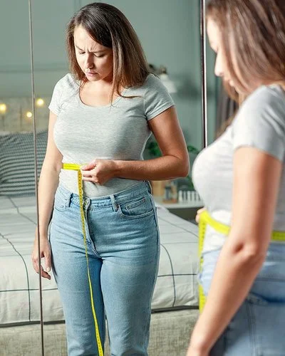 Eine Frau blickt kritisch auf das Maßband, das sie sich um die Talie gelegt hat.