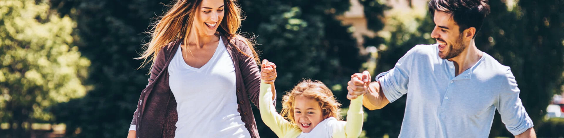 Eine glückliche Familie: Ein Vater und eine Mutter nehmen jeweils einen Arm ihrer Tochter und ziehen sie spielend hoch.