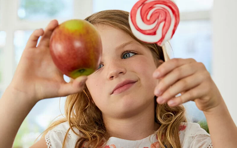 Kind hat die Wahl zwischen einem Apfel und einem süßem Lolli.