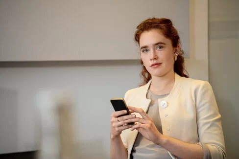 Eine Frau hat ein Smartphone in der Hand. Wie hoch der Krankenkassenbeitrag für Angestellte ist, kann sie online recherchieren. 