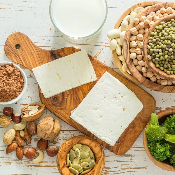 Nüsse, Hülsenfrüchte, Tofu & Co.: Vegane Proteinquellen in kleinen Schüsseln und auf Holzbrettchen verteilt auf einer Küchenarbeitsplatte.