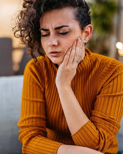 Eine junge Frau mit Mundschleimhautentzündung hält sich schmerzverzerrt das Gesicht.