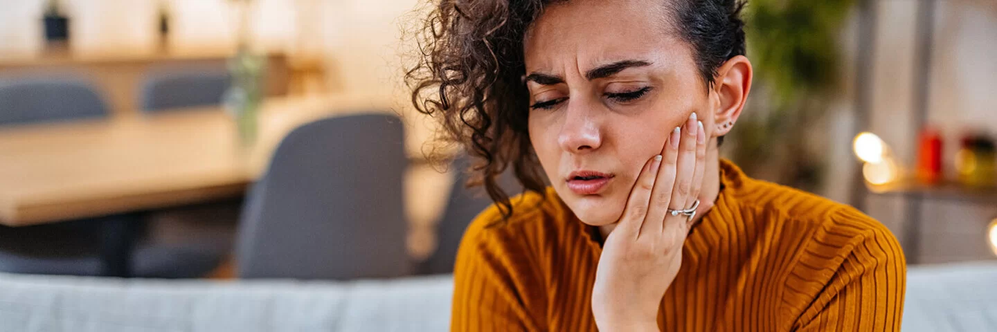 Eine junge Frau mit Mundschleimhautentzündung hält sich schmerzverzerrt das Gesicht.