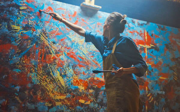 Eine Frau mit Synästhesie bemalt eine große Leinwand mit bunten Farben.