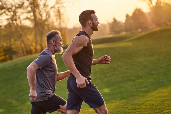 Zwei Männer laufen in sportlicher Kleidung über eine Wiese im Sonnenuntergang.