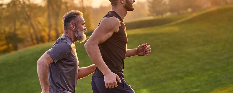 Zwei Männer laufen in sportlicher Kleidung über eine Wiese im Sonnenuntergang.