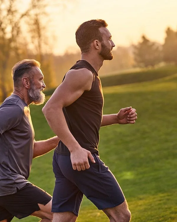 Zwei Männer laufen in sportlicher Kleidung über eine Wiese im Sonnenuntergang.