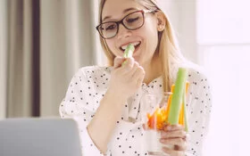 Junge Frau isst einen gesunden Low-Carb-Snack am Schreibtisch.