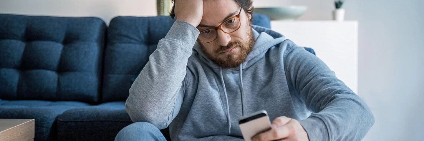 Ein Mann liest schlechte Nachrichten am Smartphone und leidet unter Doomscrolling.