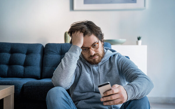 Ein Mann liest schlechte Nachrichten am Smartphone und leidet unter Doomscrolling.