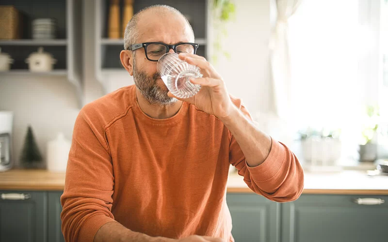 Ein Mann trinkt Wasser, das ist wichtig beim Verzehr von Flohsamenschalen.