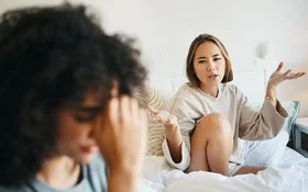 Zwei junge Frauen sitzen in einem Bett und diskutieren angestrengt.