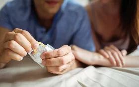 Ein Mann und eine Frau öffnen eine Kondompackung, sie praktizieren Safer Sex.