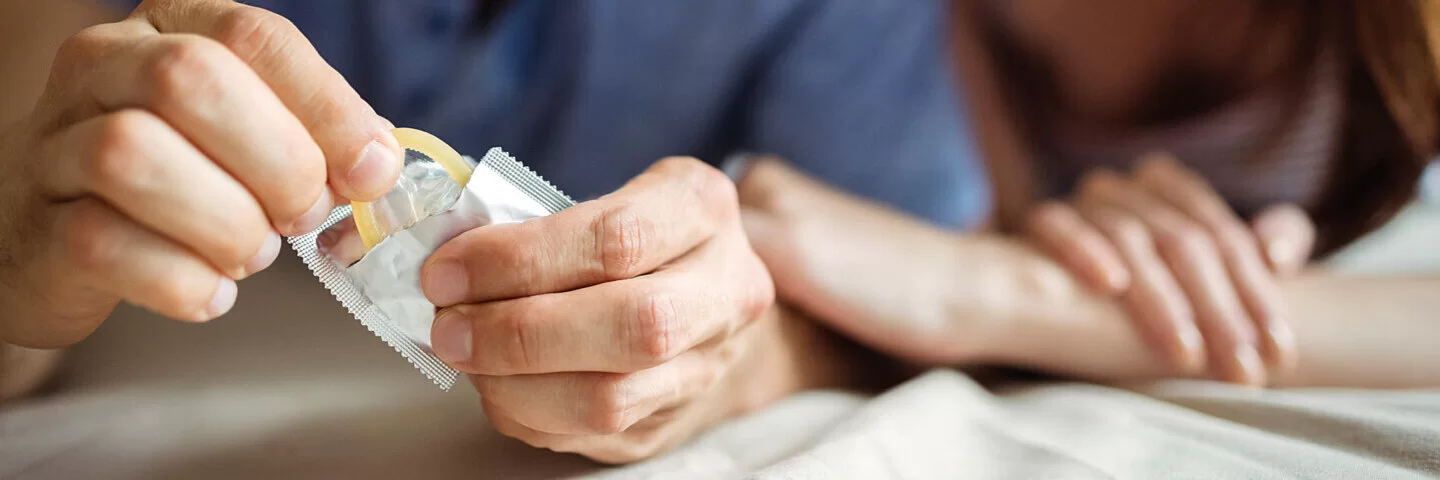 Ein Mann und eine Frau öffnen eine Kondompackung, sie praktizieren Safer Sex.