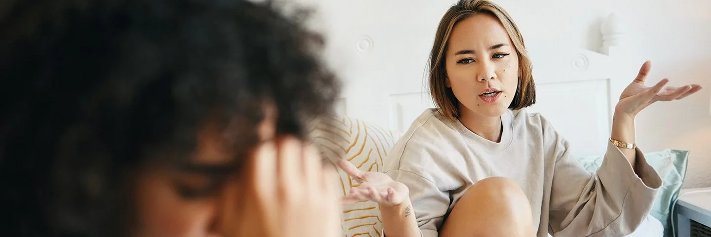 Zwei junge Frauen sitzen in einem Bett und diskutieren angestrengt.