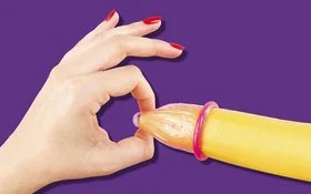 Hand mit roten Fingernägeln hält das Ende eines Kondoms auf einer Banane.