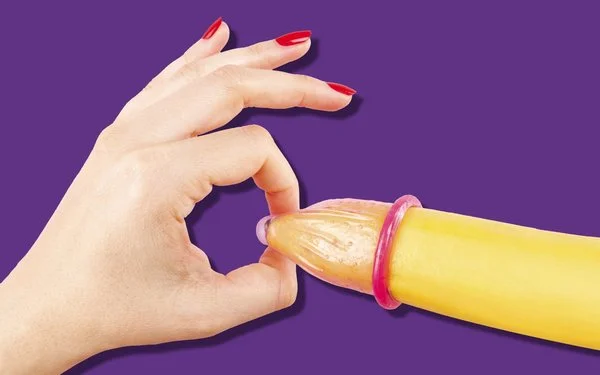 Hand mit roten Fingernägeln hält das Ende eines Kondoms auf einer Banane.