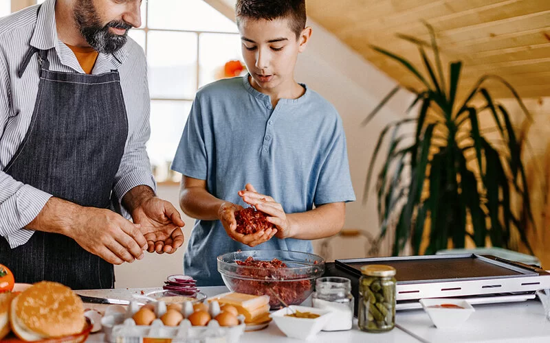 Vater und Sohn bereiten aus Hackfleisch Burgerpattys zu.