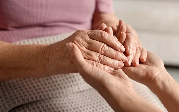 Nahaufnahme der Hände einer alten und einer jungen Frau, die ineinandergreifen.