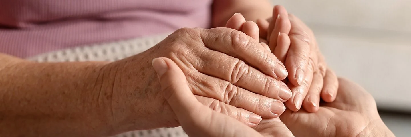 Nahaufnahme der Hände einer alten und einer jungen Frau, die ineinandergreifen.