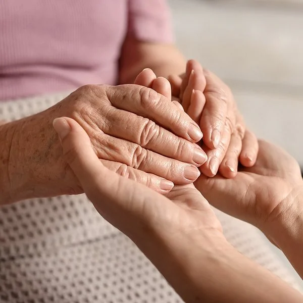 Nahaufnahme der Hände einer alten und einer jungen Frau, die ineinandergreifen.