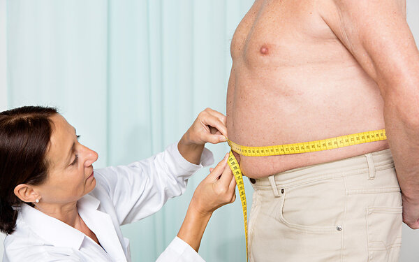 Eine Ärztin misst bei einem übergewichtigen Patienten den erhöhten Taillenumfang, der ein Symptom des metabolischen Symptoms sein kann.
