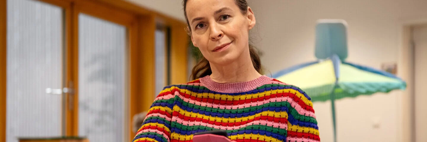 Eine Frau mit Smartphone lächelt in die Kamera.