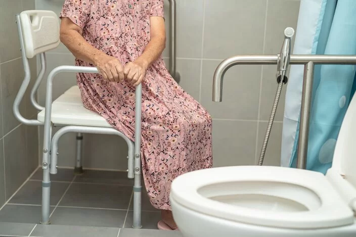 Eine Frau sitzt in der Dusche auf einem Duschstuhl.