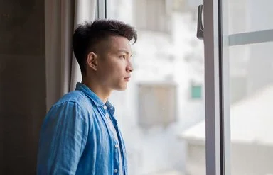 Ein junger Mann, ein Hikikomori, schaut nachdenklich aus dem Fenster.