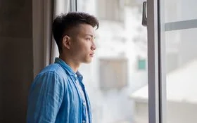 Ein junger Mann, ein Hikikomori, schaut nachdenklich aus dem Fenster.