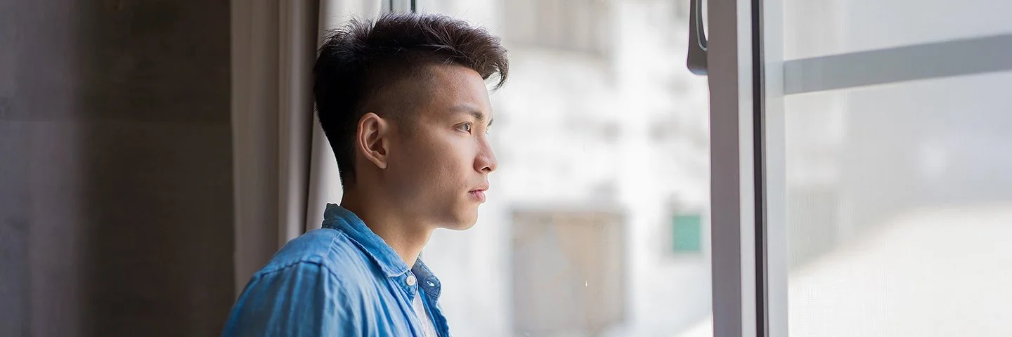 Ein junger Mann, ein Hikikomori, schaut nachdenklich aus dem Fenster.