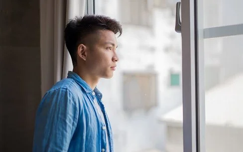 Ein junger Mann, ein Hikikomori, schaut nachdenklich aus dem Fenster.