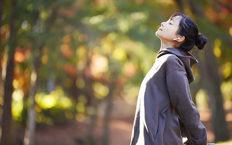 Junge Frau mit Dutt und in Sportsachen dehnt sich am Morgen im Park.