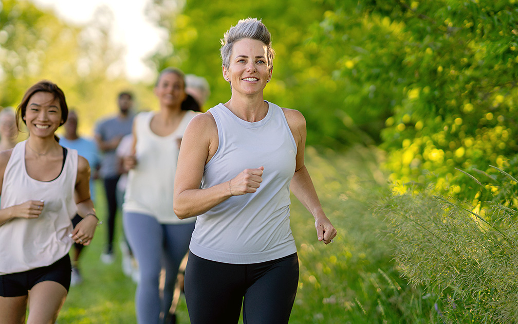 Mehrere junge bis mittelalte Frauen, die sportliche Kleidung tragen und in einer ländlichen Umgebung joggen.