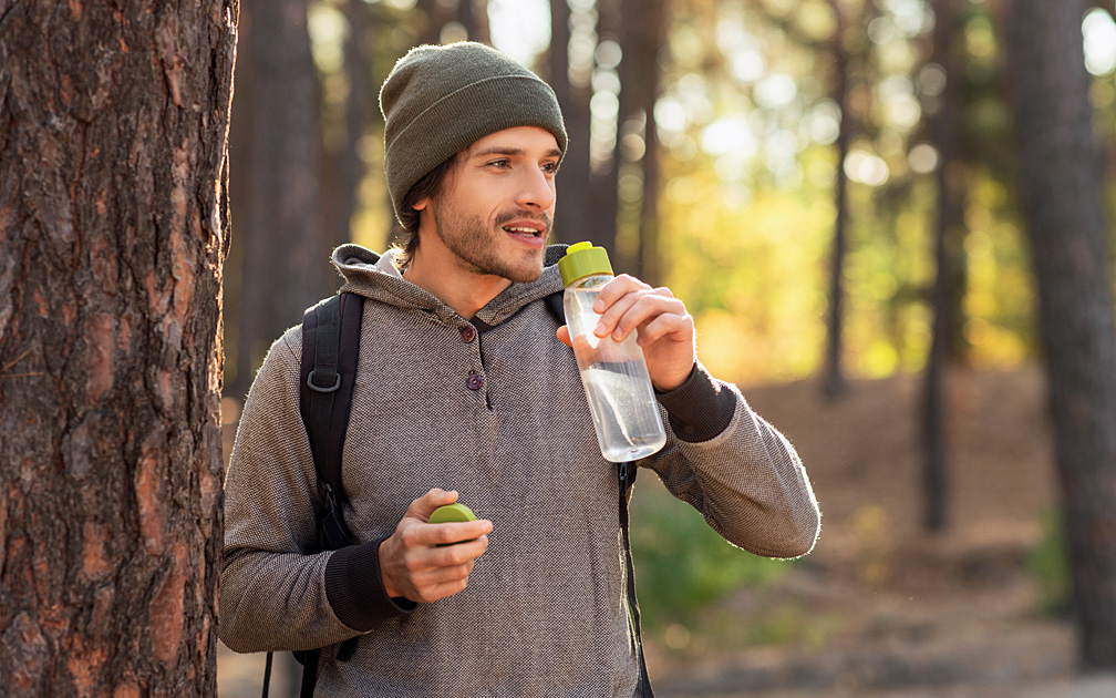 Mann ist im Wald an der frischen Luft und trinkt Wasser.