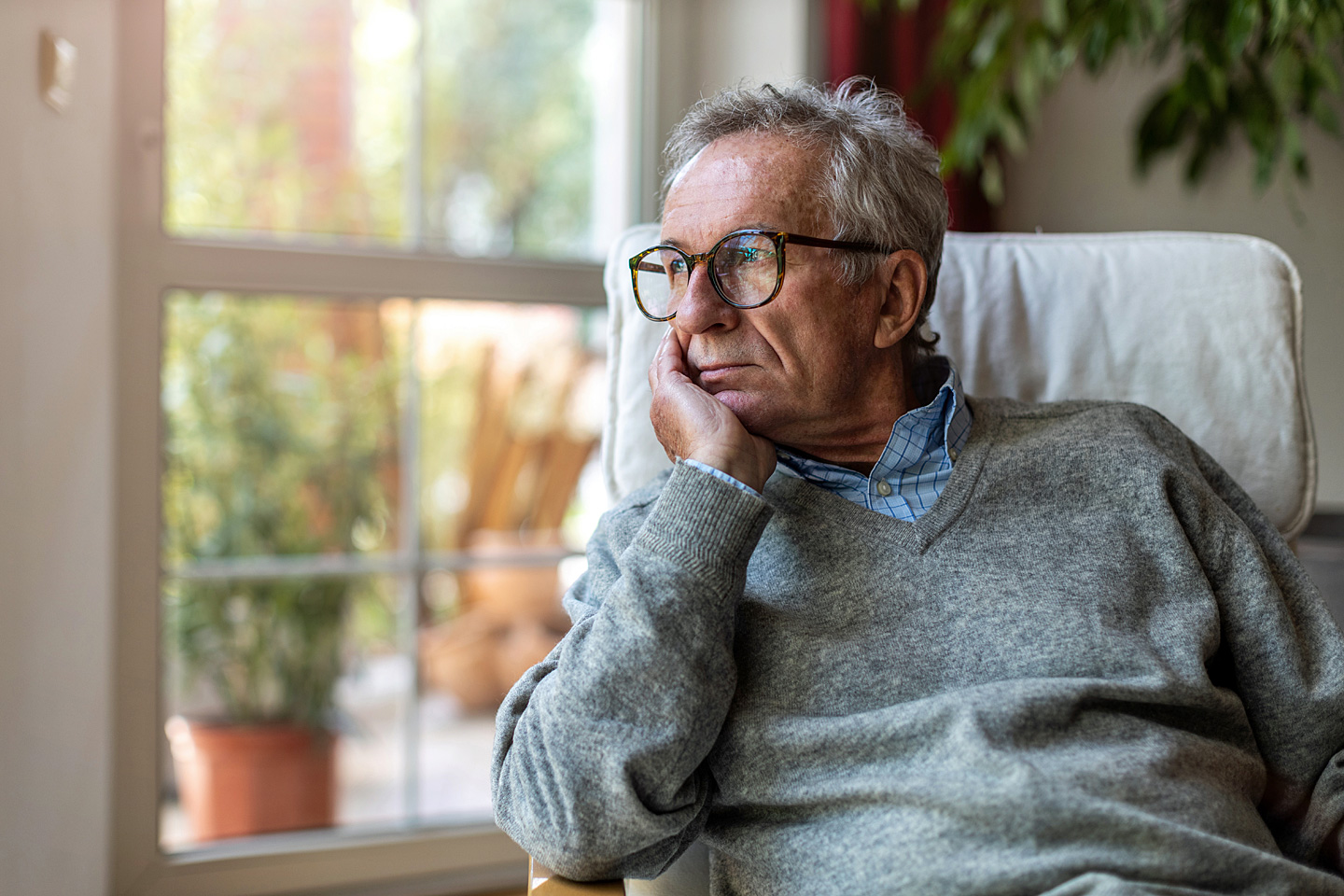 Ein älterer Mann mit Prostatakrebs steht am Fenster und blickt besorgt in die Ferne.