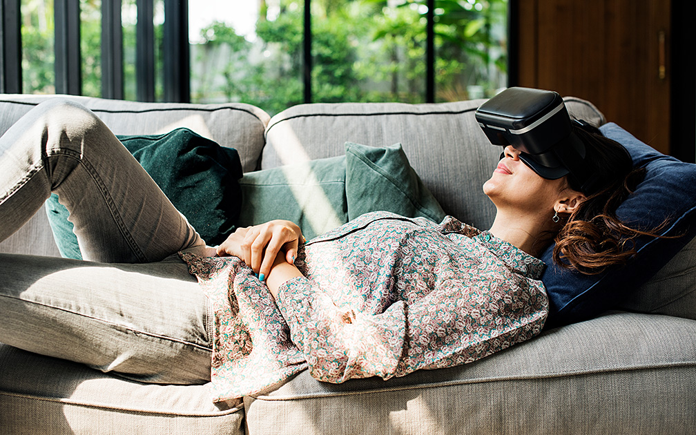 Eine Frau liegt mit einer VR-Brille entspannt auf dem Sofa.