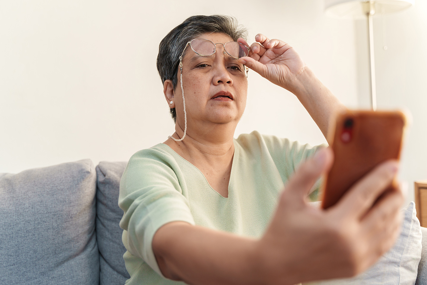 Ältere Frau leidet an Presbyopie (Alterssichtigkeit) und kann die Schrift auf ihrem Smartphone nicht mehr erkennen.