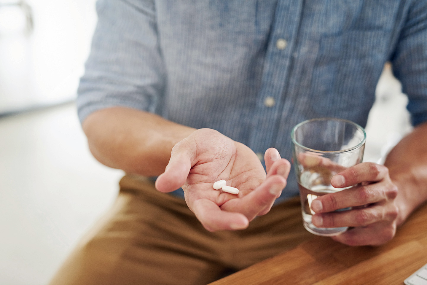 Ein Mann hält zwei Tabletten in der Hand, die er mit einem Glas Wasser zu sich nehmen möchte.