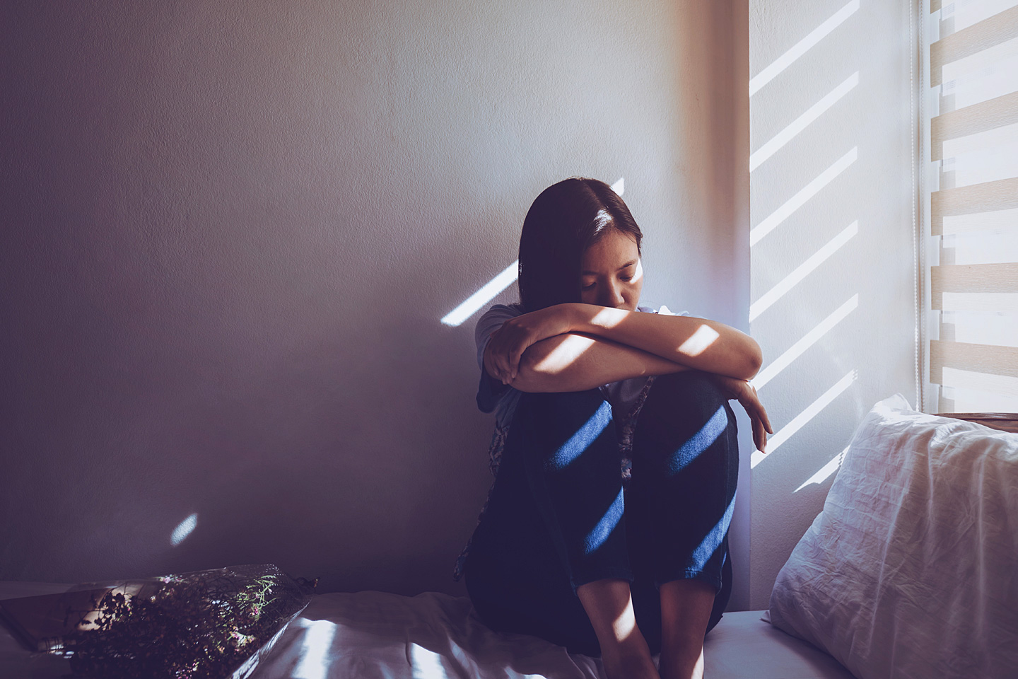 Frau mit Depressionen sitzt auf ihrem Bett vor dem Fenster.