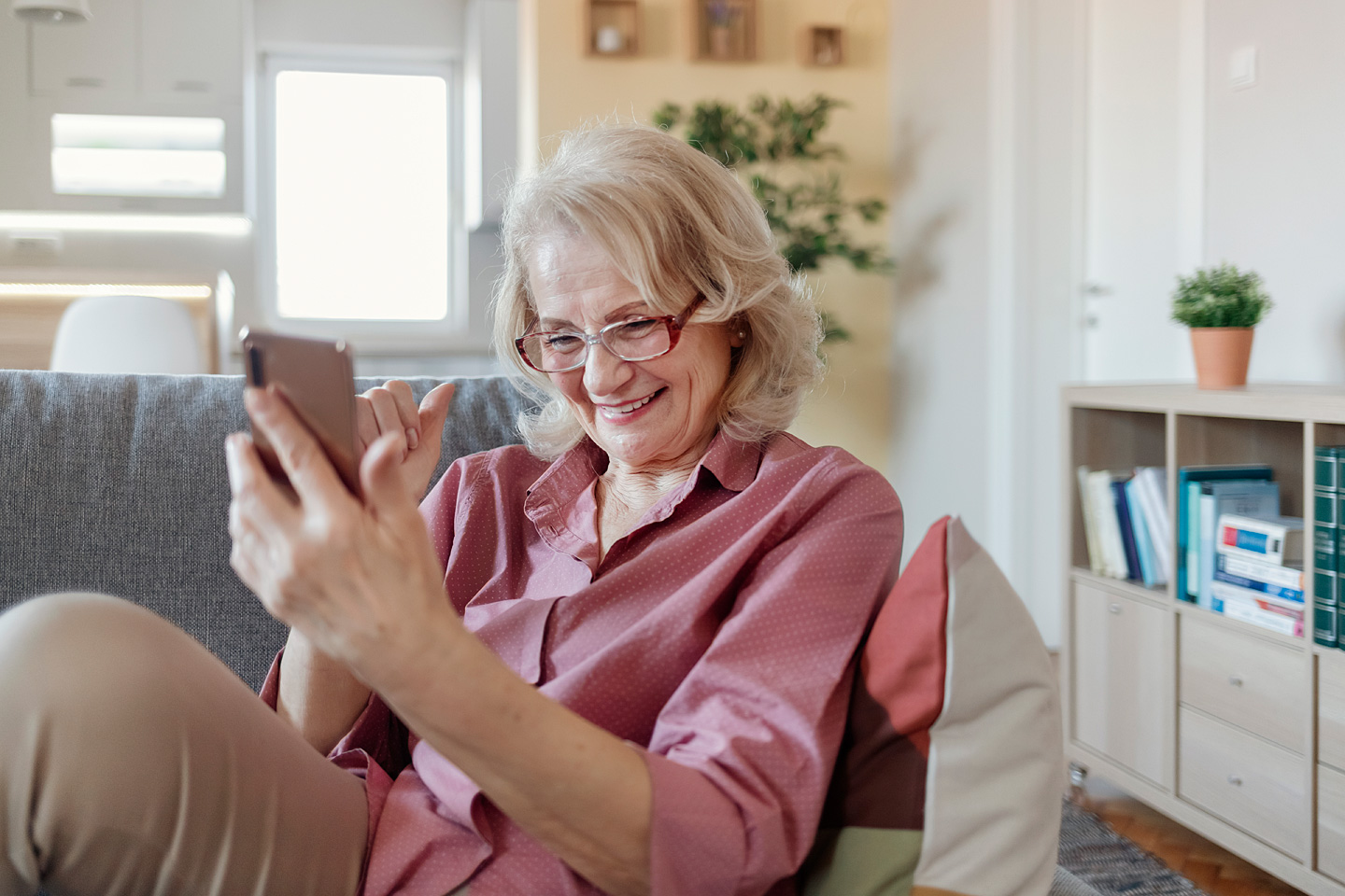 Eine ältere Frau sitzt mit dem Smartphone auf dem Sofa – und zeigt so, dass Digitalisierung auch im Alter möglich ist.