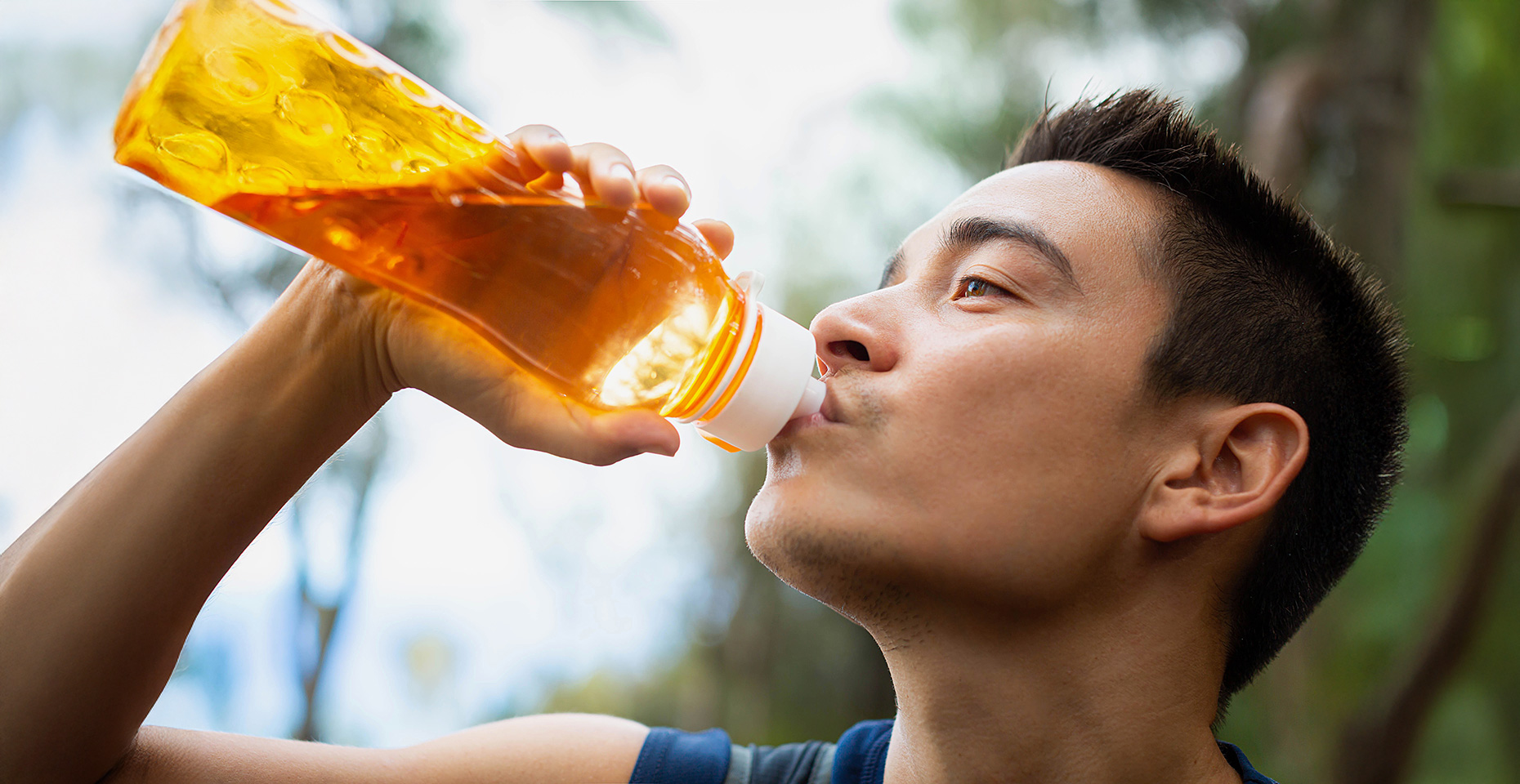 Ein junger Mann trinkt im Freien aus einer durchsichtigen, orangefarbenen Trinkflasche.