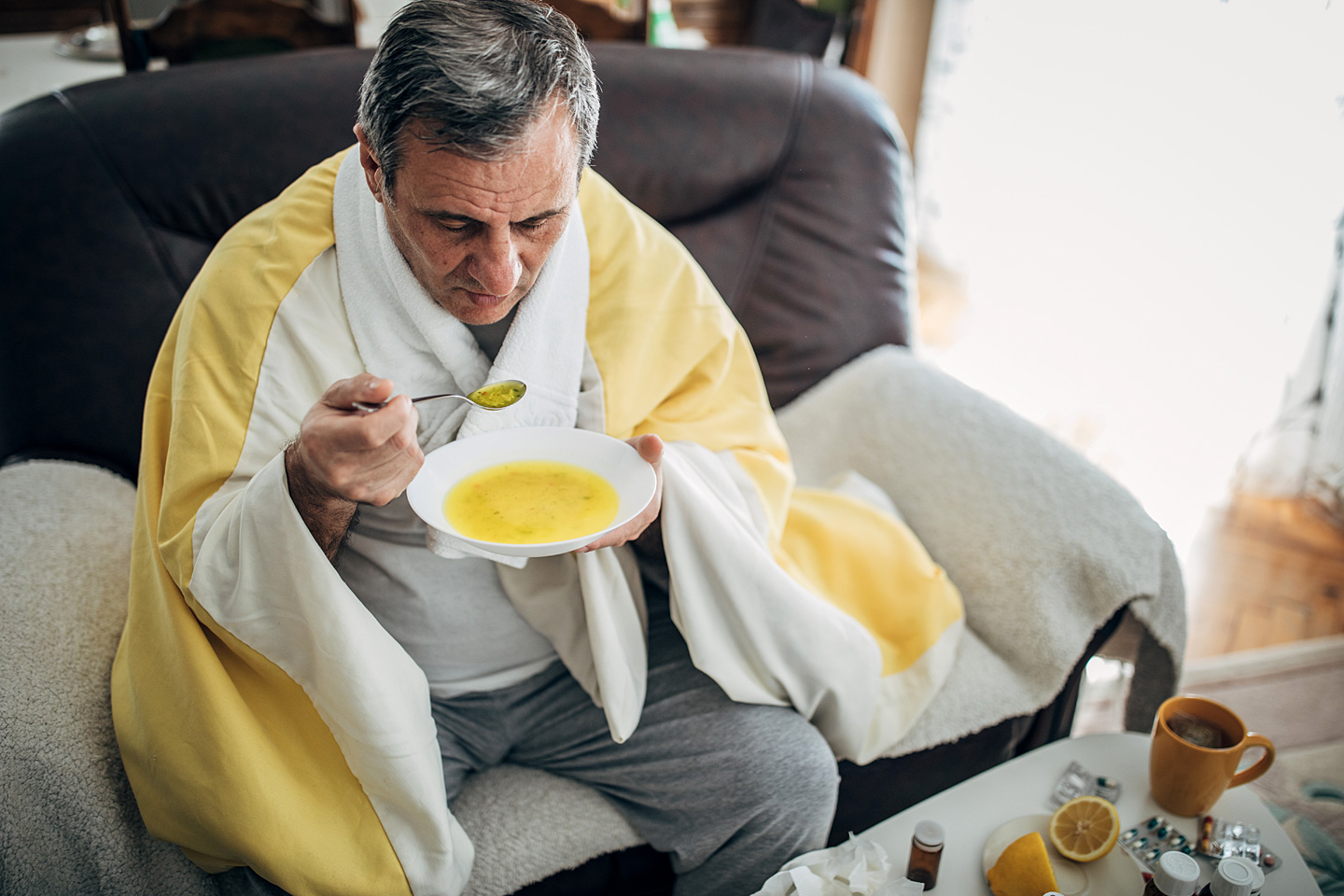 Ein Mann sitzt auf dem Sofa und löffelt eine warme Suppe.